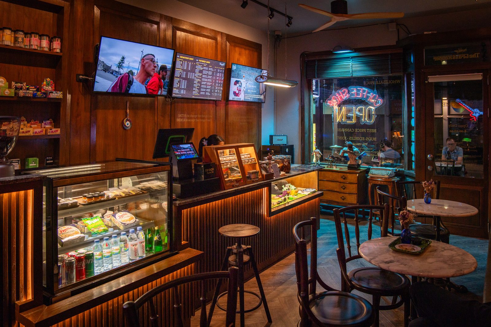 ภายในร้าน The Grasshopper ผนังไม้ ตู้โชว์กระจก ทีวีเมนูเหนือเคาน์เตอร์ และโต๊ะคาเฟ่